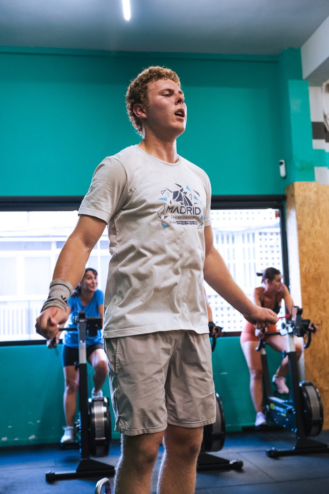 Athlete mid-workout in a gym class, with others training on BikeErgs behind